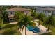 An aerial view of a blue pool, spa, light beige patio, and palm trees in the backyard of a luxury home at 13125 Casabella Dr, Windermere, FL 34786