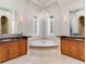 Well-lit bathroom featuring dual vanities, a soaking tub, a chandelier, and natural light from arched windows at 6143 Cartmel Ln, Windermere, FL 34786