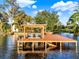 Private dock with a boat lift, ladder, and calm lake waters, surrounded by lush greenery and a blue sky at 12228 Kirby Smith Rd, Orlando, FL 32832
