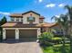Beautiful two-story home with a red tile roof, brick driveway, three-car garage, and lush tropical landscaping at 16675 Otterchase Ln, Winter Garden, FL 34787