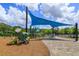 Community playground with blue sunshade, slides, and climbing structures on a wood chip ground, surrounded by trees at 6960 Audobon Osprey Cv, Harmony, FL 34773