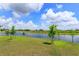 Picturesque pond view from the grassy backyard with trees under a sunny sky with fluffy white clouds at 6960 Audobon Osprey Cv, Harmony, FL 34773