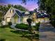 Charming yellow home with a manicured lawn with a 3-car garage on a lot with mature trees at twilight at 910 Cypress Ave, St Cloud, FL 34769