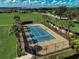 An aerial view shows a blue and tan tennis court surrounded by manicured landscaping and a fence at 223 Silver Maple Rd, Groveland, FL 34736