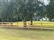 Scenic view of the property showcasing a well-maintained lawn, wooden fence, mature trees, and a charming white house in the background at 29540 Deerwood Farms Rd, Sorrento, FL 32776