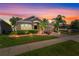 Charming single-story home featuring a well-manicured lawn, tropical landscaping, and brick accents at sunset at 4027 Sunrise Ridge Blvd, Groveland, FL 34736