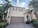 Beige two-story home featuring a two-car garage, red shutters, and tropical landscaping at 11962 Autumn Fern Ln, Orlando, FL 32827