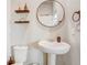 Simple half bathroom featuring a pedestal sink, round mirror, and floating shelves for storage at 2412 Gold Dust Dr, Clermont, FL 34715