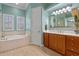 Bright bathroom features a soaking tub, wood cabinet vanity, and a large mirror, with light-toned walls and flooring at 2721 Swoop Cir, Kissimmee, FL 34741