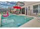 An in-ground pool featuring a screened enclosure, chairs, a red umbrella, and a view of the home's interior at 8471 Secret Key Cv, Kissimmee, FL 34747