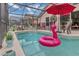A screened-in pool features a pink flamingo float, an umbrella, and lounge chairs for relaxing on sunny days at 8471 Secret Key Cv, Kissimmee, FL 34747