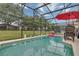 An in-ground pool featuring a screened enclosure, chairs, a red umbrella, and a view of the grassy backyard at 8471 Secret Key Cv, Kissimmee, FL 34747