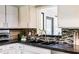 Close up of kitchen sink with black countertops, tile backsplash and white cabinets at 120 W Trade Winds Rd, Winter Springs, FL 32708