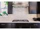 Close-up of gas cooktop and tile backsplash in kitchen featuring stainless steel appliances and dark cabinetry at 13828 Tybee Beach Ln, Orlando, FL 32827