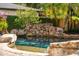 A beautiful stone waterfall feature cascading into a sparkling backyard pool, surrounded by greenery and privacy hedges at 1665 Temple Dr, Winter Park, FL 32789