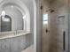 Elegant bathroom featuring a glass shower, arched mirror, marble countertops, and beautiful vanity with stylish sconces at 16812 Vinci Way, Bella Collina, FL 34756