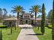 Stately stone home featuring a tiled roof, arched entryway, and lush landscaping with mature palms at 16812 Vinci Way, Bella Collina, FL 34756