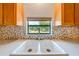 Double sink featuring a garden view, light wood cabinets and a stone backsplash at 3975 Rambler Ave, St Cloud, FL 34772