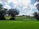 Picturesque golf course view with mature trees, lush greenery, and cloudy blue skies at 6084 Masters Blvd, Orlando, FL 32819