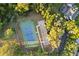 Aerial view of a tennis court and parking bordered by mature landscaping and a home's roofline at 7351 Spring Mountain Ln, Yalaha, FL 34797
