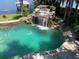 Swimming pool with stone surround features a rock waterfall and lush, tropical landscaping at 1105 Lake Nettie Dr, Eustis, FL 32726
