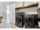 Laundry room with a modern, front-load washer and dryer next to a wooden shelf and doorway at 13320 Magnolia Valley Dr, Clermont, FL 34711