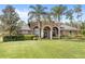 Stunning front view of the tan home with lush green lawn and palm trees at 2825 Lakeshore Dr, Mount Dora, FL 32757