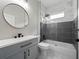Modern bathroom with a stylish vanity, round mirror, sleek black fixtures, and a combined shower and tub with gray and white tiling at 826 Jade Forest Ave, Orlando, FL 32828