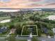 An aerial shot captures a home bordered in white outline amid lush trees, a golf course, and a tranquil lake at sunset at 6054 Tarawood Dr, Orlando, FL 32819