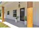 Welcoming front porch with a black front door, wood columns, modern light fixture, and potted plants at 6725 Sw 131St Cir, Ocala, FL 34481