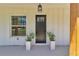 Welcoming front porch with a black front door, wood columns, modern light fixture, and potted plants at 6725 Sw 131St Cir, Ocala, FL 34481