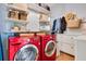 A modern laundry room featuring a red washer and dryer, overhead storage, and tiled floors at 12636 Hammock Pointe Cir, Clermont, FL 34711