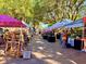 Outdoor market featuring tents with local produce and handmade goods on a tree-lined street at 76 Oakdale St, Windermere, FL 34786
