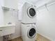Well-lit laundry room featuring a stacked washer and dryer, utility sink, and overhead shelving for organized storage at 12822 Moss Park Ridge Dr, Orlando, FL 32832