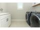 Modern laundry room with front loading navy washer and dryer and white cabinets, plus a light-filled window at 13617 Haulover Beach Ln, Orlando, FL 32827