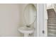 Powder room features pedestal sink and a round mirror next to a staircase at 15210 Chapter Way, Winter Garden, FL 34787
