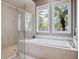 A pristine bathroom featuring a glass shower, a soaking tub, and bright windows with tropical views at 8581 Lake Nona Shore Dr, Orlando, FL 32827