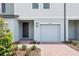 Close-up of a townhouse with a brick paver driveway, gray door and garage door, and manicured bushes at 16434 Bird Of Paradise Ave, Clermont, FL 34714