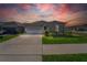 Charming single-story home featuring a two-car garage, well-manicured lawn, and inviting curb appeal under a vibrant sunset sky at 820 Overpool Ave, Davenport, FL 33896