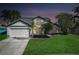 Charming two-story home featuring a well-manicured lawn, mature trees, and a spacious two-car garage at dusk at 11160 Sylvan Pond Cir, Orlando, FL 32825