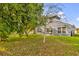 View of the backyard with a lush lawn, mature trees, and a patio with sliding glass doors at 1851 Wimbledon St, Kissimmee, FL 34743