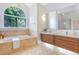 Elegant bathroom featuring a soaking tub beneath a large arched window, complemented by wood vanities at 13124 Filly Ct, Windermere, FL 34786