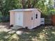 Exterior view of a pink storage shed with a ramp and white trim surrounded by a green lawn and wooden fence at 1620 Carolyn Ct, St Cloud, FL 34769