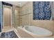 A bathtub and glass enclosed shower are surrounded by beige tiling and accented with decorative wallpaper at 1767 Piedmont Pl, Lake Mary, FL 32746