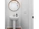 A modern bathroom with a sleek pedestal sink, wood floors, and a round mirror at 1120 Parma Cir, Lake Mary, FL 32746