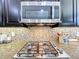Close-up of a stainless steel microwave and gas cooktop with a decorative tile backsplash at 1078 Vinsetta Cir, Winter Garden, FL 34787
