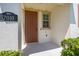 Welcoming front porch featuring a classic brown door, natural light from a window, and lush greenery at 7010 Broomshedge Trl, Winter Garden, FL 34787