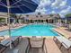 A spacious pool area features ample seating with lounge chairs and umbrellas and a large clubhouse in the background at 7010 Broomshedge Trl, Winter Garden, FL 34787