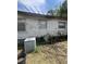 A shot of the home's exterior with its faded white siding, old AC unit, and yard with visible debris at 7506 Mott Ave, Orlando, FL 32810