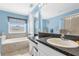 Well-lit bathroom with blue walls, a soaking tub, a glass-enclosed shower, and a white vanity with dark countertop at 9112 Grey Moss Dr, Orlando, FL 32832